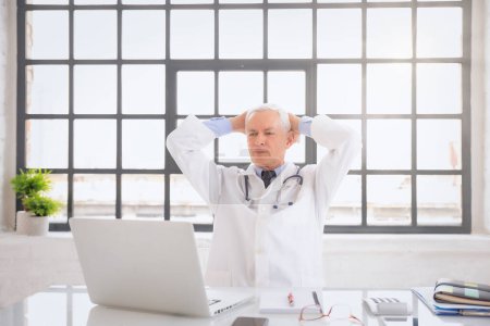 Porträt eines männlichen Arztes am Schreibtisch. Altenpfleger arbeitet im Krankenhaus. Er trägt Laborkittel. 