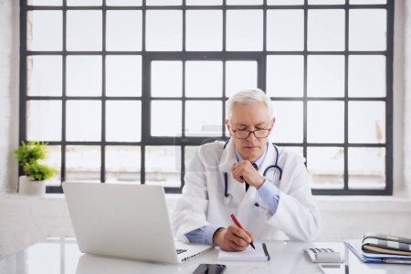 Porträt eines männlichen Arztes am Schreibtisch. Altenpfleger arbeitet im Krankenhaus. Er trägt Laborkittel und schaut nachdenklich.