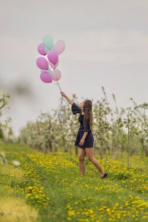 Photo for Girl with balloons in a field with blooming apple orchards - Royalty Free Image