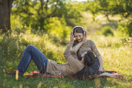 Photo for Young couple sitting in nature and listening to music with headphones - Royalty Free Image