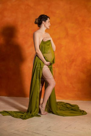 Photo for Pregnant Woman on an orange background covered with a green cloth - Royalty Free Image