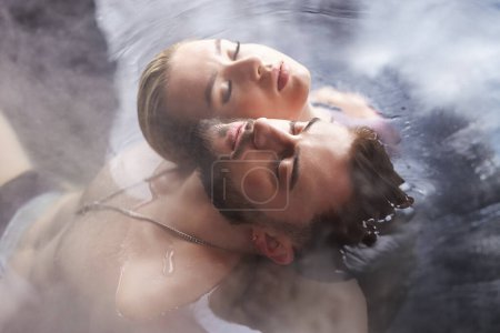 Photo for A young couple sits in a vat filled with water with their backs to each other - Royalty Free Image