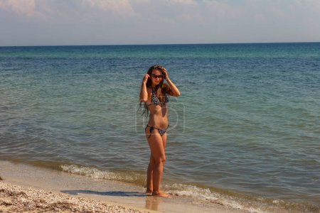 Photo for A girl in a swimsuit and sunglasses stands on the background of the sea - Royalty Free Image