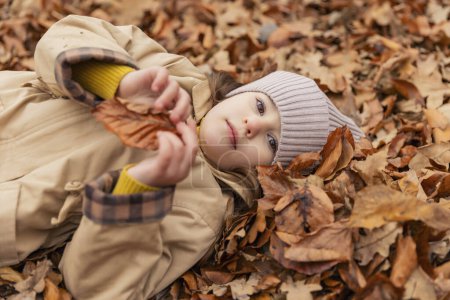 Photo for Portrait of a little girl lying in fallen autumn leaves - Royalty Free Image