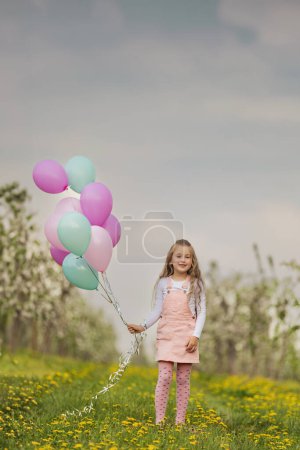Photo for Girl with colorful balloons in a blooming garden with trees - Royalty Free Image