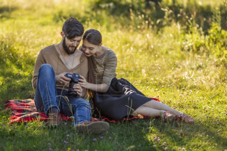 Photo for Young couple sits in nature and looks at the camera at the resulting picture - Royalty Free Image
