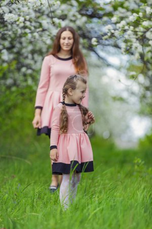Photo for Mother and daughter walk through a blooming apple orchard - Royalty Free Image