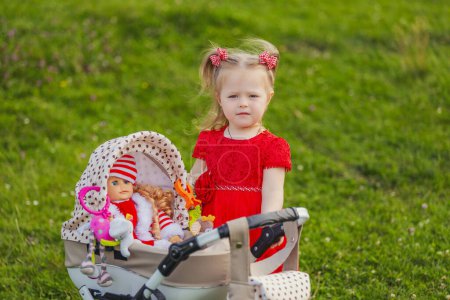 Photo for A child with a toy stroller and a doll is playing in nature - Royalty Free Image