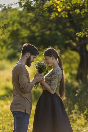 Téléchargez les photos : Couple dans la nature avec des fleurs sauvages, sentant un bouquet - en image libre de droit
