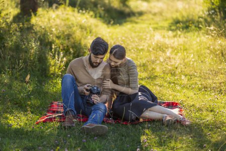 Photo for Young couple relaxing in nature and looking at photos on a camera - Royalty Free Image