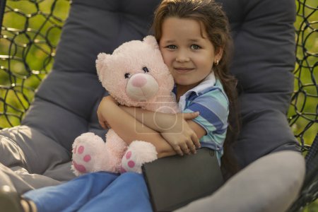Photo for Child hugging a teddy bear while sitting in a hanging chair - Royalty Free Image