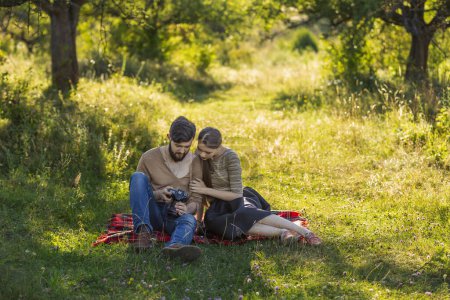 Photo for Young couple relaxing in nature and looking at photos on a camera - Royalty Free Image