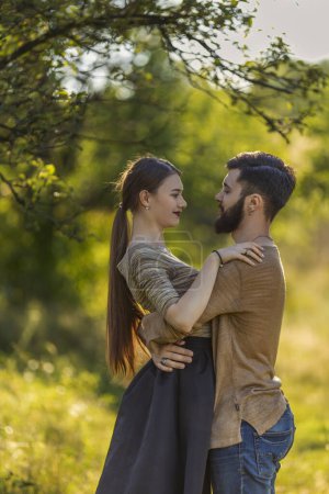 Photo for Young couple, illuminated by the backlit sun, hugging in nature - Royalty Free Image
