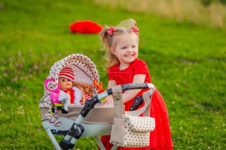 Photo for Little girl plays with a doll and a stroller on the lawn - Royalty Free Image