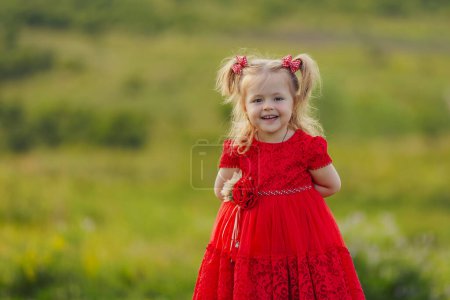 Photo for Little girl in a red dress walks on the lawn - Royalty Free Image
