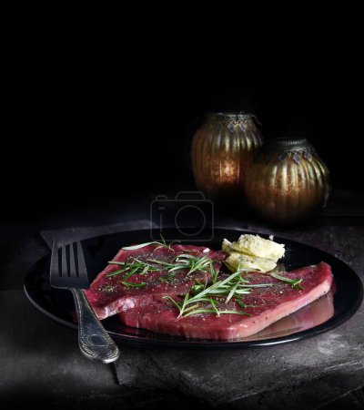 Photo for Uncooked flash fry steak fillets prepared for cooking with rosemary and butter garnish and seasoning. Generous accommodation for negative copy space for text etc. - Royalty Free Image