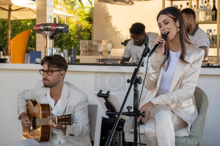 Photo for QUINTA DO LAGO, PORTUGAL - 26th JUNE 2022: Band duo singer and guitar player called Beatriz playing in a beach bar restaurant in Quinta do Lago. - Royalty Free Image