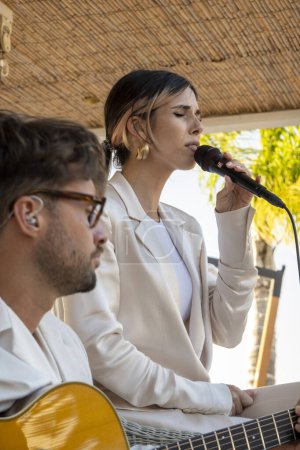 Photo for QUINTA DO LAGO, PORTUGAL - 26th JUNE 2022: Band duo singer and guitar player called Beatriz playing in a beach bar restaurant in Quinta do Lago. - Royalty Free Image