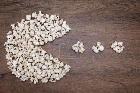Photo for A pile of popcorn in the shape of a pacman on a wooden background. Popcorn in the shape of a popular digital game model. Classic crunchy snack in the form of popcorn for watching TV - Royalty Free Image