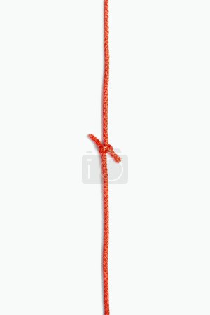 Téléchargez les photos : Les deux extrémités d'une corde rouge sont attachées dans un nœud sur un fond vertical blanc. Corde en nylon rouge avec un nœud au centre. Espace libre pour le texte et les annonces - en image libre de droit