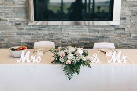 Téléchargez les photos : La table des mariés dans le restaurant est décorée avec des fleurs et des signes avec l'inscription Mr et Mrs. Belle table de jeunes mariés avec nappe blanche et fleurs - en image libre de droit