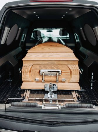 Photo for A wooden coffin stands in a black hearse. A simple wooden coffin in a black car. Funeral and farewell ceremony. Close-up photo. - Royalty Free Image