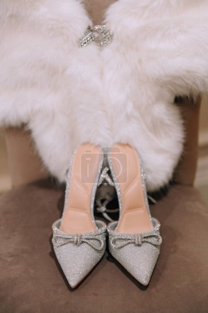 Bride's high-heeled shoes and white fur stole. The bride's wedding dress consists of shoes and a fur cape. Beautiful sparkling shoes of the bride on her wedding day