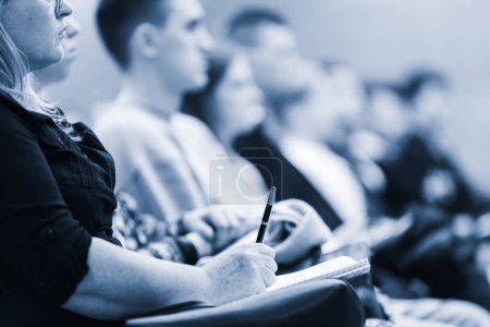 Photo for Female hands holding pen and notebook, making notes at conference lecture. Event participants in conference hall. Blue toned greyscale image - Royalty Free Image
