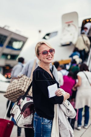 Photo for Cheerful woman holding carry on luggage queuing to board the commercial airplane. - Royalty Free Image