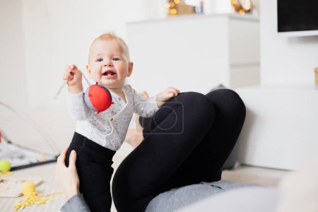 Photo for Happy family moments. Mother lying comfortably on childrens mat watching and suppervising her baby boy playinghis in living room. Positive human emotions, feelings, joy. - Royalty Free Image