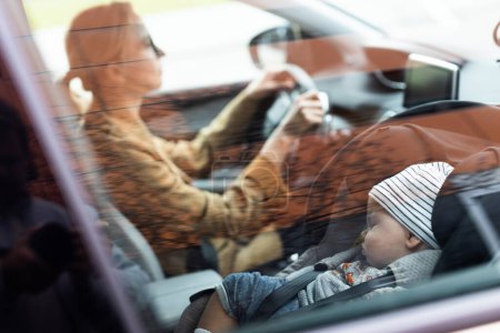 Foto de Madre concentrándose en conducir un coche familiar haciendo recados mientras su bebé duerme en un asiento de bebé junto a su sitio - Imagen libre de derechos