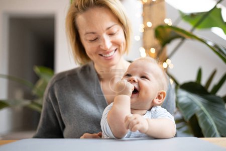 Photo for Portrait of young mother cuddling her adorable little child while sitting at the table at home. Sensory stimulation for baby development. - Royalty Free Image