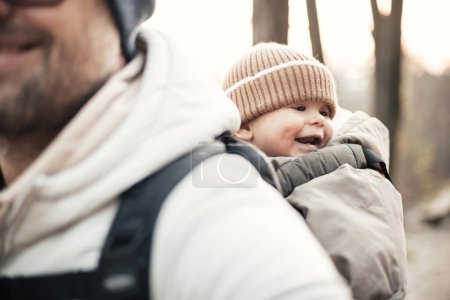 Téléchargez les photos : Père sportif portant son fils en bas âge portant une combinaison d'hiver et un bonnet dans un sac à dos portant une randonnée dans la forêt d'automne - en image libre de droit
