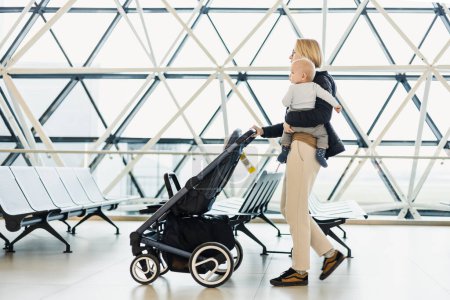 Photo for Mother carying his infant baby boy child, pushing stroller at airport departure terminal moving to boarding gates to board an airplane. Family travel with baby concept - Royalty Free Image