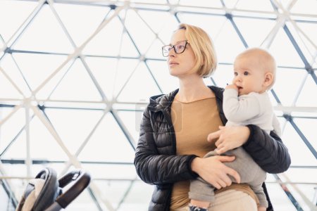 Photo for Mother carying his infant baby boy child, pushing stroller at airport departure terminal waiting at boarding gates to board an airplane. Family travel with baby concept - Royalty Free Image