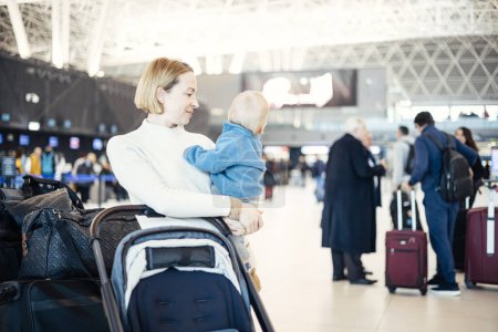 Téléchargez les photos : Mère voyageant avec son bébé garçon enfant, marchant, poussant bébé poussette et chariot à bagages à la gare de l'aéroport. Concept de voyage avec enfant - en image libre de droit