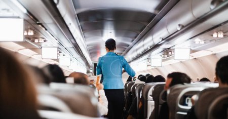 Foto de Interior del avión con pasajeros en asientos y azafata en uniforme caminando por el pasillo, sirviendo a las personas. Concepto de servicio de vuelo economía comercial - Imagen libre de derechos