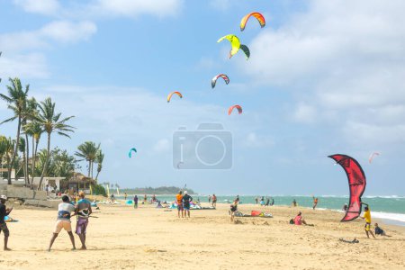 Téléchargez les photos : Foule de sportifs actifs profitant de vacances de kitesurf et d'activités par une journée ensoleillée parfaite sur la plage de sable tropical de Cabarete en République dominicaine - en image libre de droit