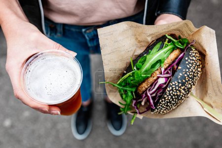 Großaufnahme einer Frau, die einen leckeren vegetarischen Burger mit Bio-Lachs und selbstgebrautem IPA-Bier auf einem urbanen Street-Food-Festival in Ljubljana, Slowenien, in Händen hält