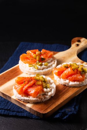 Photo for Healthy food non gluten Smoked Salmon canape Smoked salmon with rice cracker on wooden board on black slate stone - Royalty Free Image