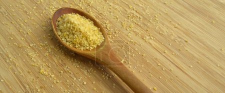Téléchargez les photos : Grain de daliya de blé craquelé sec dans une cuillère en bois, sur une planche à découper en bambou - en image libre de droit