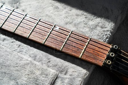 Close-up of electric guitar steel strings and fretboard made of rosewood rest on a plush guard
