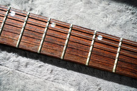 Nahaufnahme von Stahlsaiten der E-Gitarre und Griffbrett aus Palisander ruhen auf einem Plüschgitter