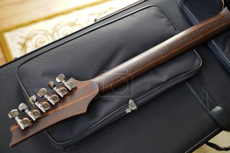 Primer plano del cabezal de cuerdas de acero para guitarra eléctrica y diapasón hecho de palisandro en un protector de felpa