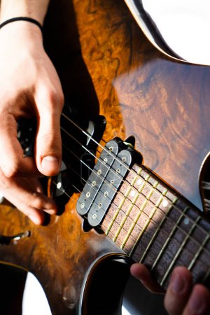 Manos de un músico caucásico tocando la guitarra eléctrica, tocando la guitarra eléctrica de madera de color marrón brillante