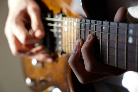 Foto de Manos de un músico caucásico tocando la guitarra eléctrica, tocando la guitarra eléctrica de madera de color marrón brillante - Imagen libre de derechos