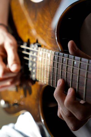 Hands of a Caucasian musician playing electric guitar, playing bright brown color wooden electric guitar