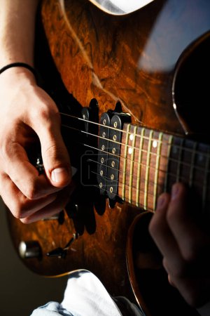 Hands of a Caucasian musician playing electric guitar, playing bright brown color wooden electric guitar