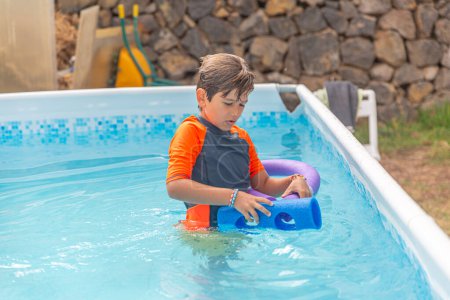 Photo for Cheerful young boy playing with blue water noodles in a pool on a bright day - Royalty Free Image
