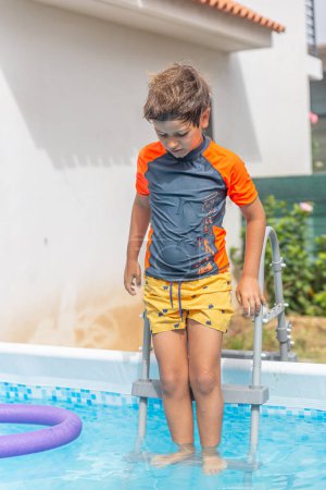 Photo for Young boy with a determined look climbing out of a pool, a swim noodle floating behind on a sunny day - Royalty Free Image